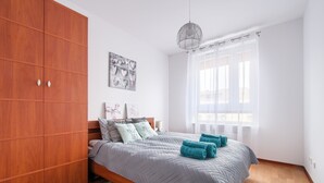 A bedroom with a wooden wardrobe, a bed with grey bedding, a decorative wall piece, and a window with sheer curtains.
