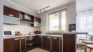 A modern kitchen with dark wood cabinets, a white countertop, a built-in microwave, a coffee maker, and a window with a view of buildings outside.