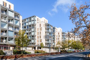 Ein modernes Apartmenthaus mit mehreren Balkonen, blauem Himmel und einer Straße mit geparkten Autos.