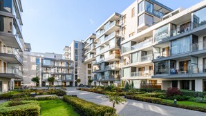 Moderni kerrostalo, jossa on useita parvekkeita, keskeinen sisäpiha ja hyvin hoidettu puutarha.