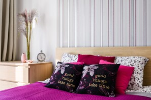 Ein Schlafzimmer mit Bett, Kissen, einem Nachttisch, einer Vase und einer Wand mit vertikalen Streifen.