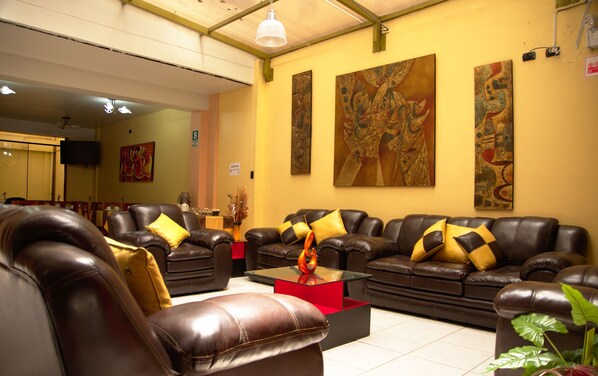 A spacious living room with leather sofas, a glass coffee table, and large abstract paintings on the walls. - Hotel Melanys (Cusco)