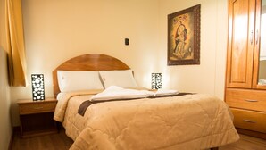 Una cama bien hecha con colcha color beige, cabecera de madera y dos mesitas de noche con lámparas decorativas.
