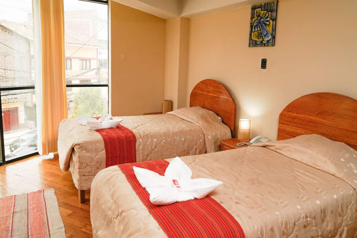 Ett hotellrum med två sängar, ett stort fönster, en tavla på väggen och en sänggavel i trä.