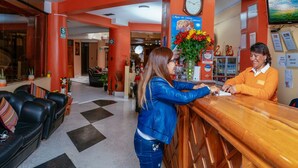 Un área de recepción con mostrador, un reloj y un televisor en la pared mostrando el mensaje 