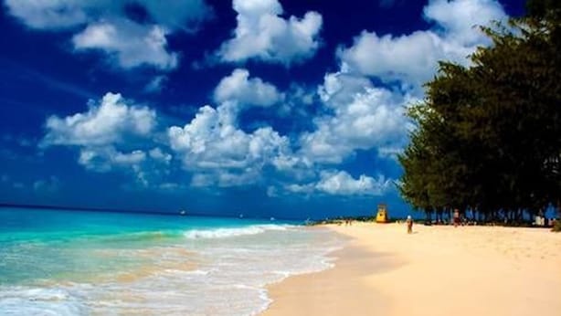 Ein Strand mit klarem, blauem Wasser, sandigem Ufer und einigen Personen.