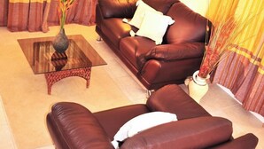 Ein Wohnzimmer mit braunem Ledersofa, einem Glastisch und gelben Vorhängen.