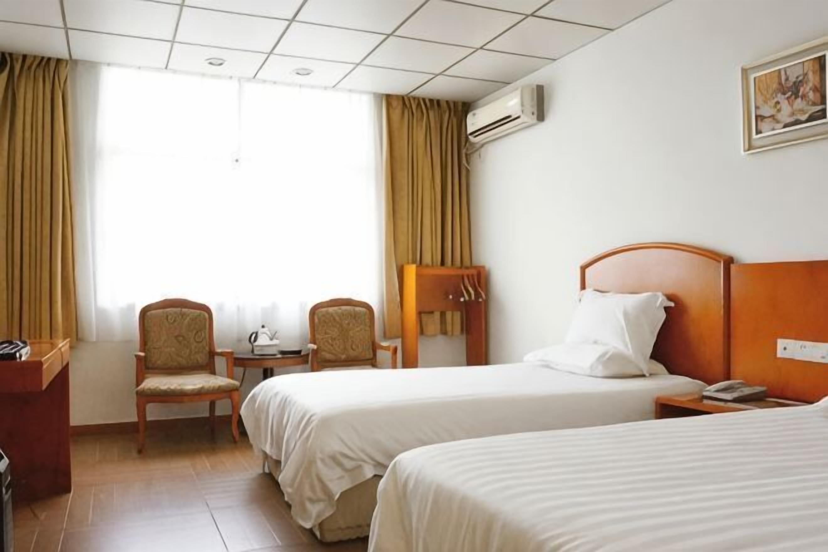Habitación de hotel con dos camas, un escritorio, sillas y una ventana con cortinas.