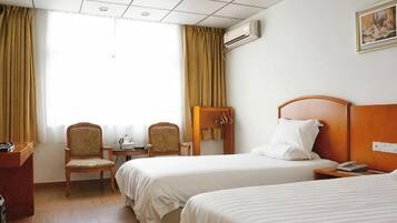 Habitación de hotel con dos camas, un escritorio, sillas y una ventana con cortinas.