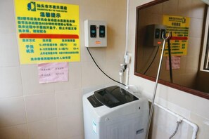 A bathroom with a white washing machine, a mirror, and a wall-mounted electrical outlet. - Shantou Buyetian Hotel (SHANTOU)