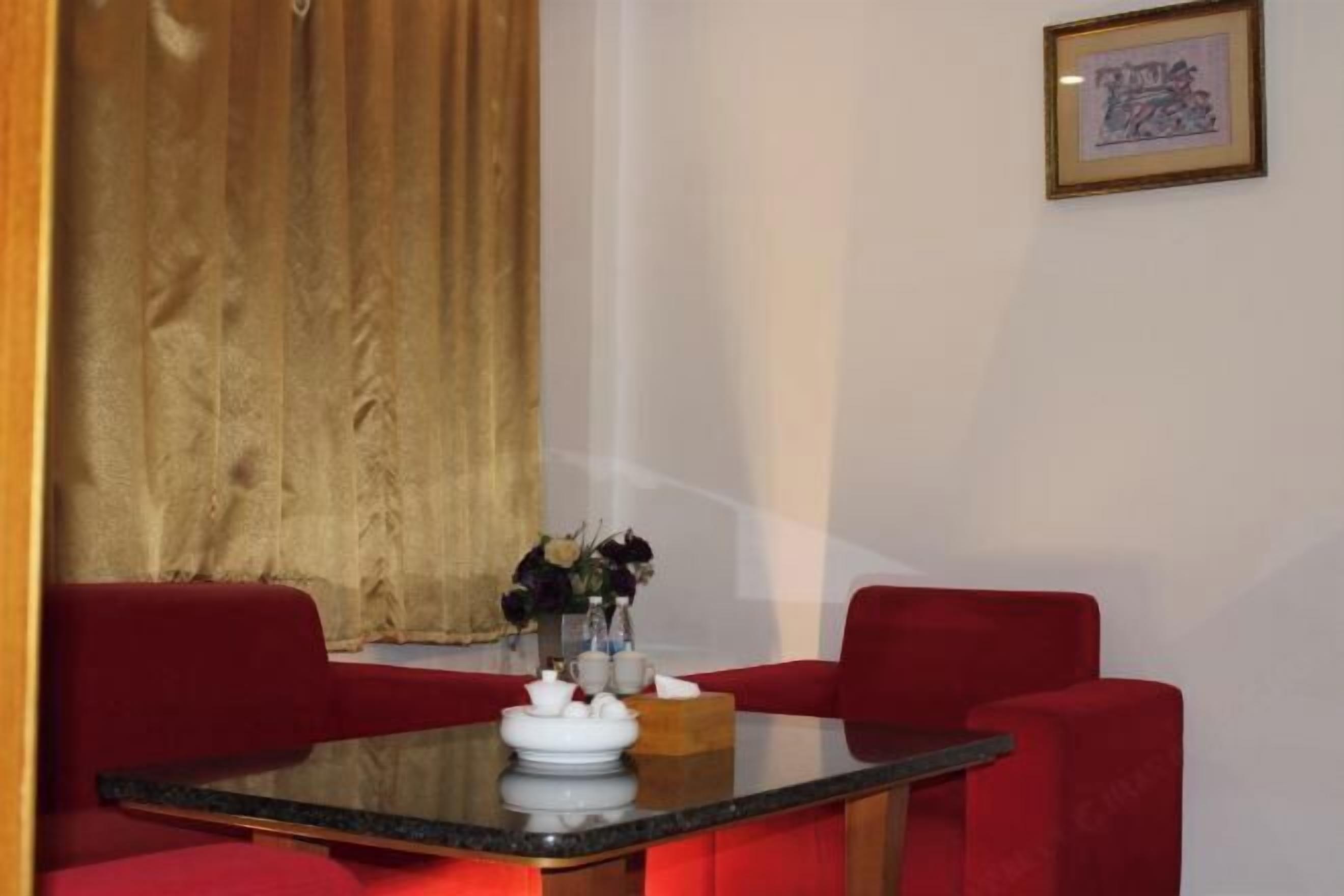 A dining area with a glass table, red upholstered chairs, a vase with flowers, and a framed picture on the wall.