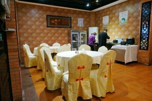 A dining area with round tables and chairs, a refrigerator, and a person in the background. - Shantou Buyetian Hotel (SHANTOU)