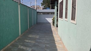 Un couloir étroit, doté d’un sol carrelé et de murs verts, mène à une zone délimitée par une clôture blanche et agrémentée d’une petite plante.