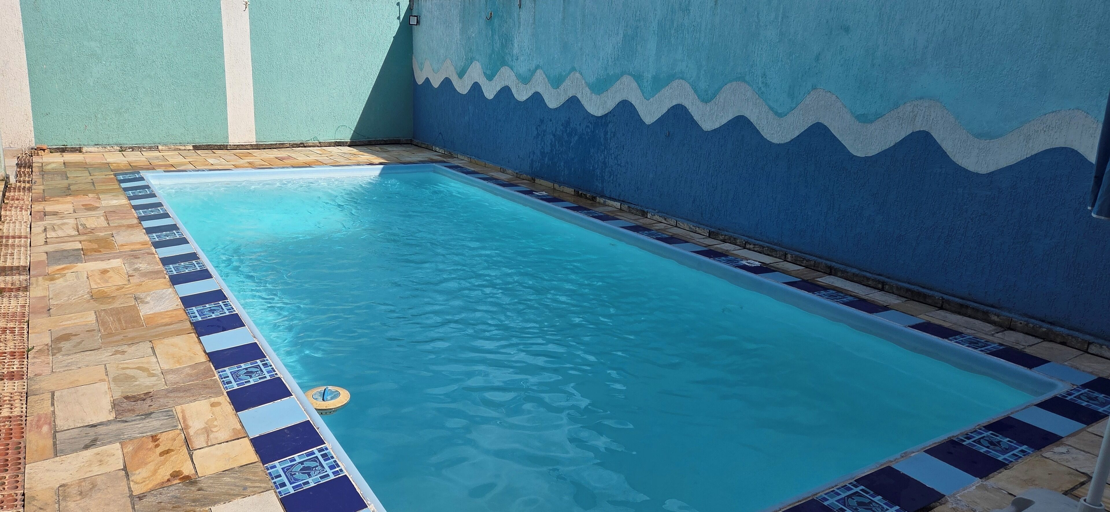 Ein rechteckiger Pool mit einer gefliesten Kante, umgeben von einer Steindeck und einer Wand mit einem Wellenmuster.