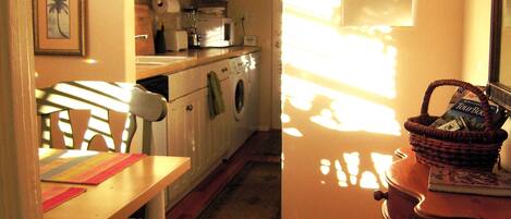 A narrow kitchen with a washing machine, a dining table with chairs, and a small table with a basket.