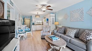 Un salon comprenant un canapé, une table basse et des coussins à motifs. On y trouve également un coin repas avec une table et des chaises. La pièce est dotée d’un ventilateur de plafond et de décorations murales.
