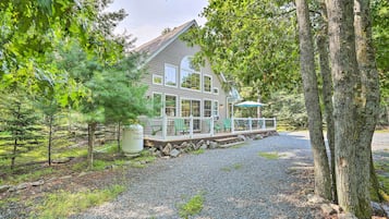 A house with a covered porch, surrounded by trees and a gravel driveway.
