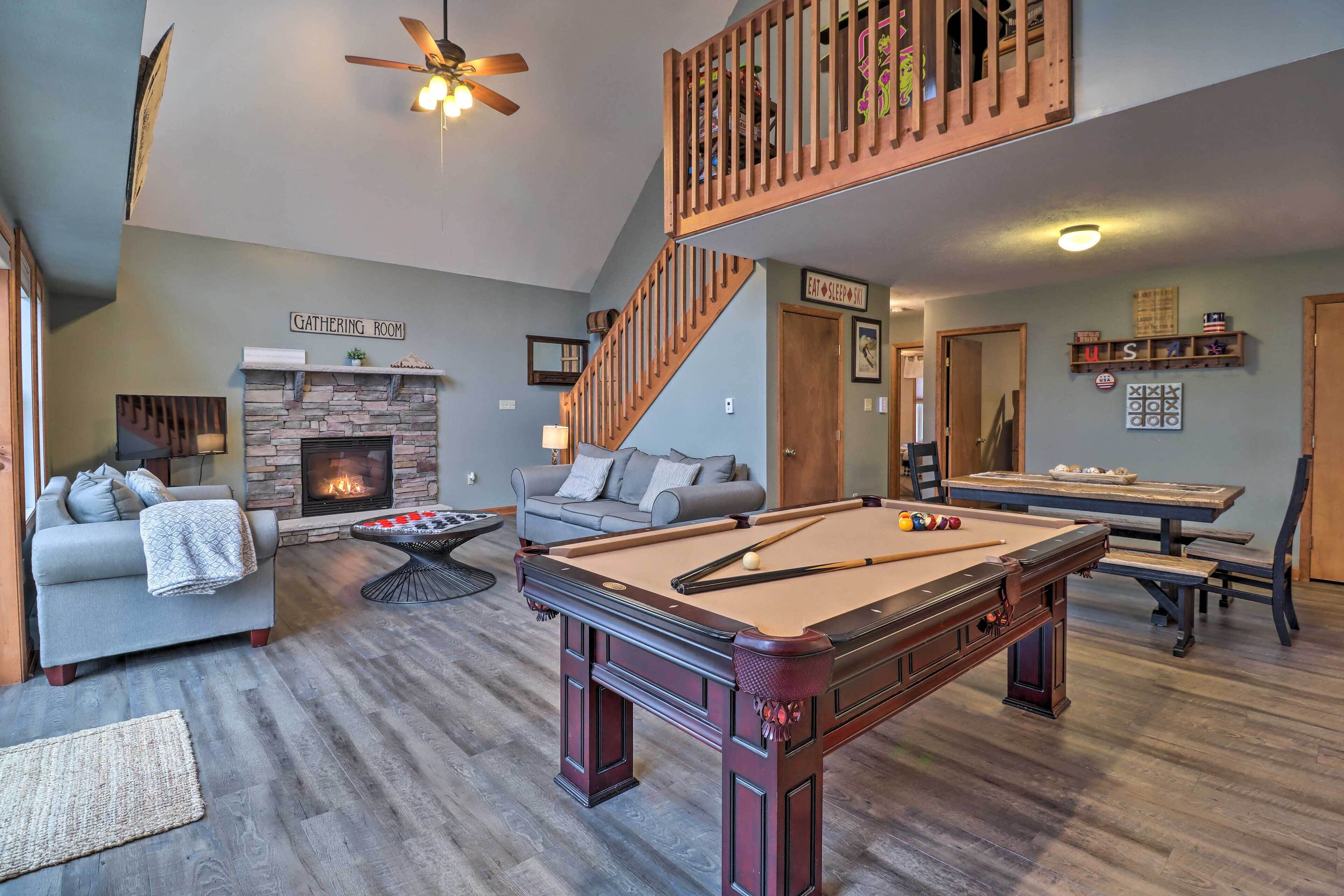 A spacious living room with a pool table, a fireplace, a sofa, and a staircase.