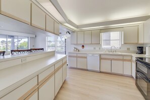 Une cuisine moderne avec des meubles blancs, un lave-vaisselle, une cuisinière et une fenêtre équipée de stores.