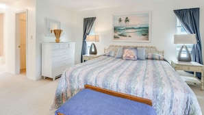 Un dormitorio con cama, mesitas de noche, cómoda, un cuadro y ventilador de techo.