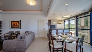 A modern living room with a gray sofa, dining table, and chairs. There is a painting on the wall and a door leading to another room. - VERY TOP! Beautiful APARTMENT Ocean Front HIGH STANDARD (Meia Praia)