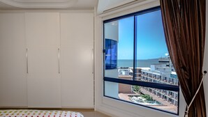 Ein Schlafzimmer mit großem Fenster, weißem Kleiderschrank und einem Bett mit farbenfroher Bettdecke.