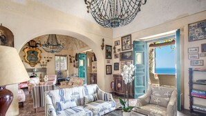 A spacious living room with a chandelier, a sofa, armchairs, and a view of the sea through an open door. - AMORE RENTALS - Villa San Giacomo – Historic Luxury Villa with Sea View (Positano)
