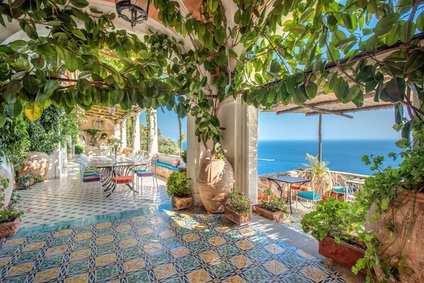 A terrace with a tiled floor, outdoor furniture, potted plants, and a view of the sea.