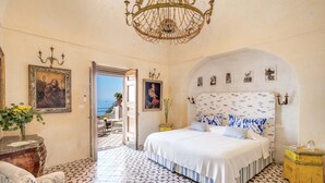 A bedroom with a large bed, a chandelier, and a view of the sea through an open door. - AMORE RENTALS - Villa San Giacomo – Historic Luxury Villa with Sea View (Positano)