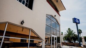 A building with a large glass entrance, a parking area, and a blue sign on a pole. - Hotel Go Inn (Monclova)