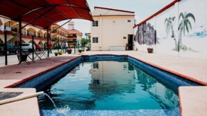 A swimming pool with a red canopy, a mural of palm trees, and a building with a beige facade. - Hotel Go Inn (Monclova)