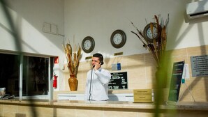 A hotel reception desk with clocks, a fire extinguisher, and a sign indicating room rates. - Hotel Go Inn (Monclova)