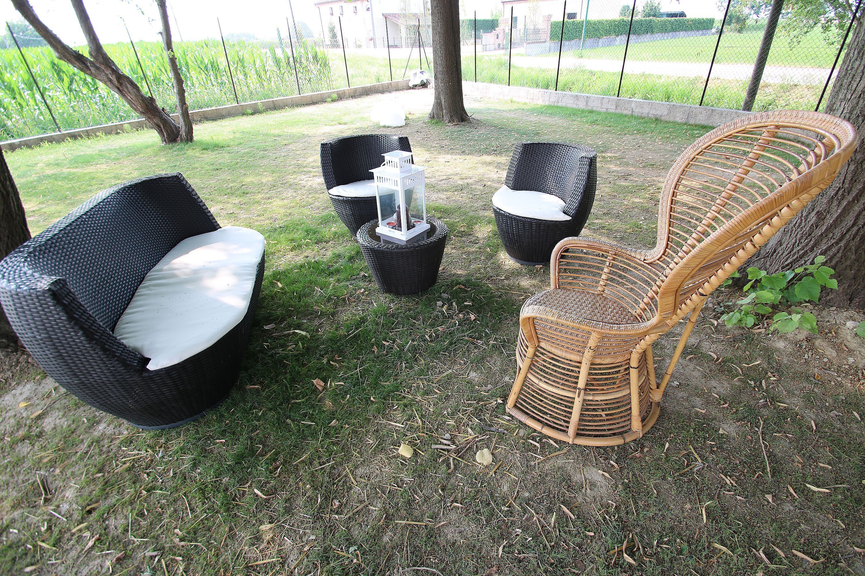 Un espace aménagé dans le jardin, avec des chaises et une table en osier, entouré de pelouse et d’arbres.