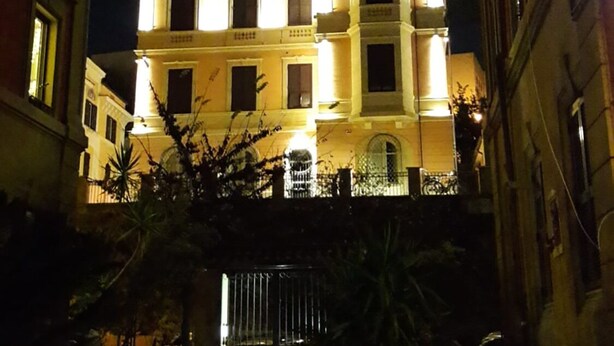 A multi-story building with illuminated windows and a gated entrance, surrounded by potted plants. - Enchanting apartment 2 minutes away from the Vatican Museums (Roma)