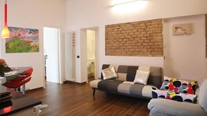 A living room with a sofa, a dining area with a table and chairs, a brick accent wall, and a colorful painting. - Enchanting apartment 2 minutes away from the Vatican Museums (Roma)