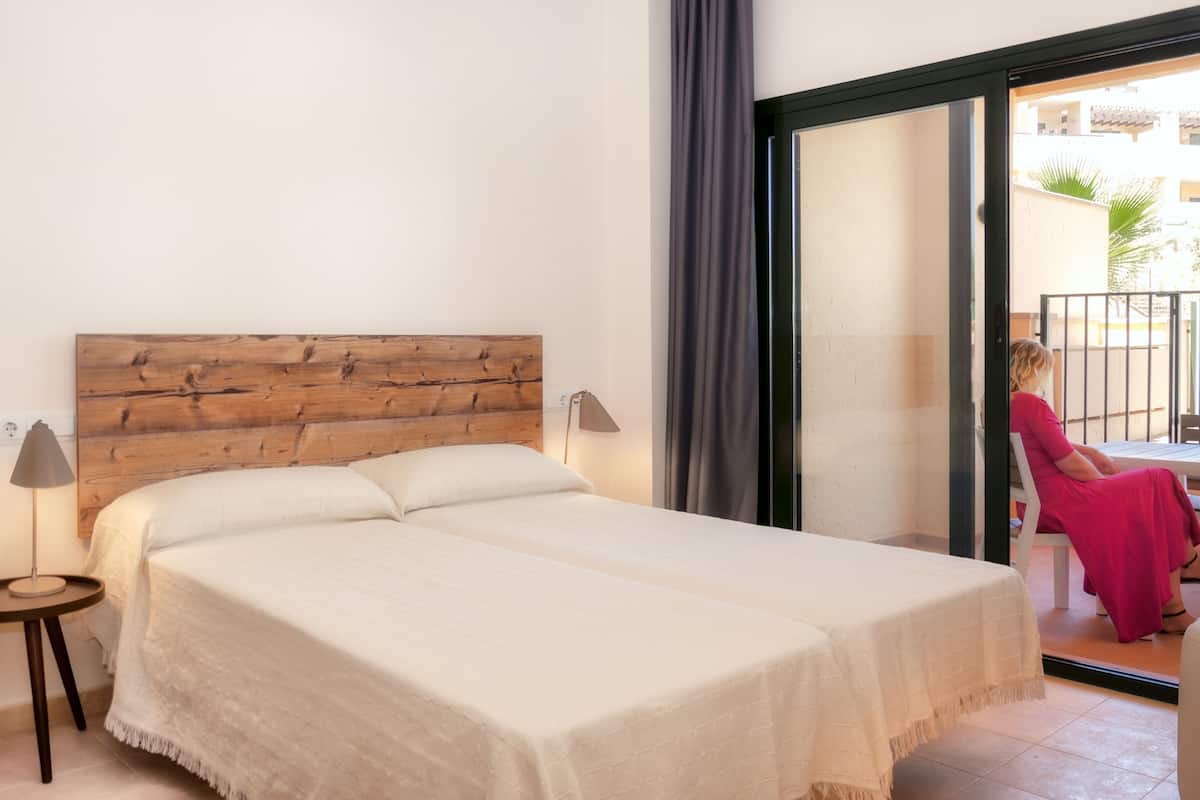 A bedroom with a wooden headboard, a bed with white linens, a small bedside table, and a lamp.