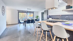 A modern kitchen with a central island, a dining area with blue chairs, and a large window with a view of trees. - Villa Fortuna - in historic town Buje with 4 bedrooms and a pool, near the beach by MyWaycation (Kaštel)