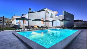 A modern pool area with lounge chairs and umbrellas, surrounded by a large building with large windows. - Villa Fortuna - in historic town Buje with 4 bedrooms and a pool, near the beach by MyWaycation (Kaštel)