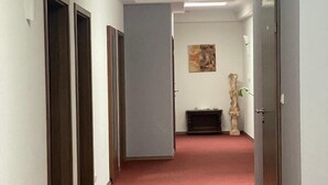 A hallway with a red carpet, white walls, and a ceiling light. There are doors on both sides and a statue in the center. - Hotel Isabella (Frankfurt)
