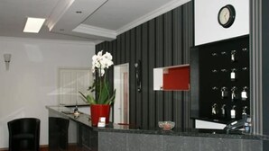 A reception area with a counter, a clock, and a wall-mounted display. - Hotel Isabella (Frankfurt)
