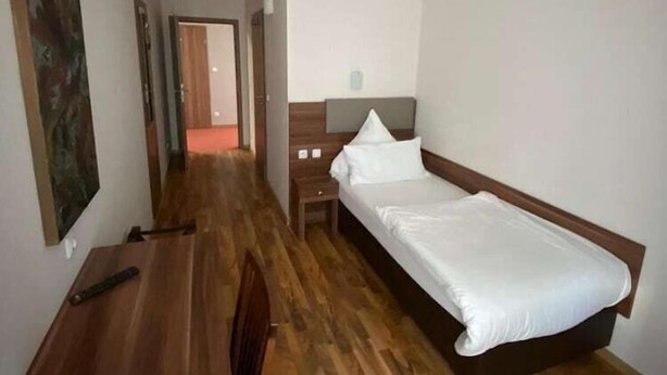 A hotel room with a wooden floor, a bed with white bedding, a desk with a chair, and a painting on the wall. - Hotel Isabella (Frankfurt)