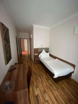 A hotel room with a wooden floor, a bed with white bedding, a desk with a chair, and a painting on the wall. - Hotel Isabella (Frankfurt)