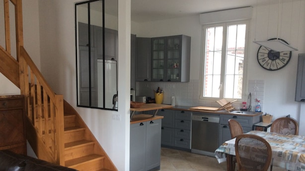 A kitchen with grey cabinets, a wooden staircase, and a dining area with a table and chairs.