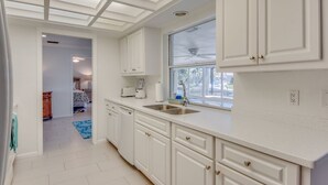 A modern kitchen with white cabinetry, a large window, and a ceiling fan.