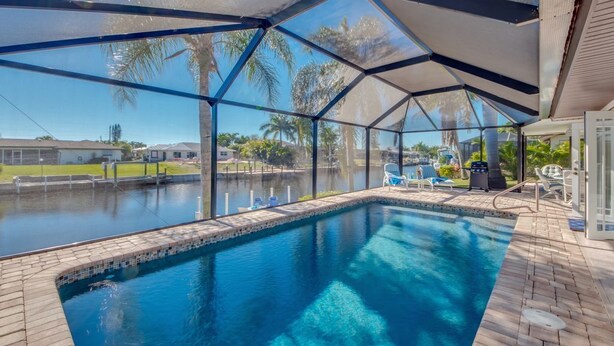 A covered swimming pool with clear views of palm trees and a distant house.