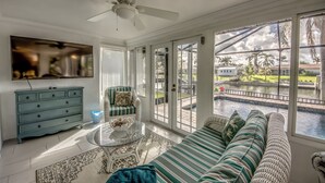 A spacious living room with a large window, a ceiling fan, a sofa, a coffee table, and a TV.