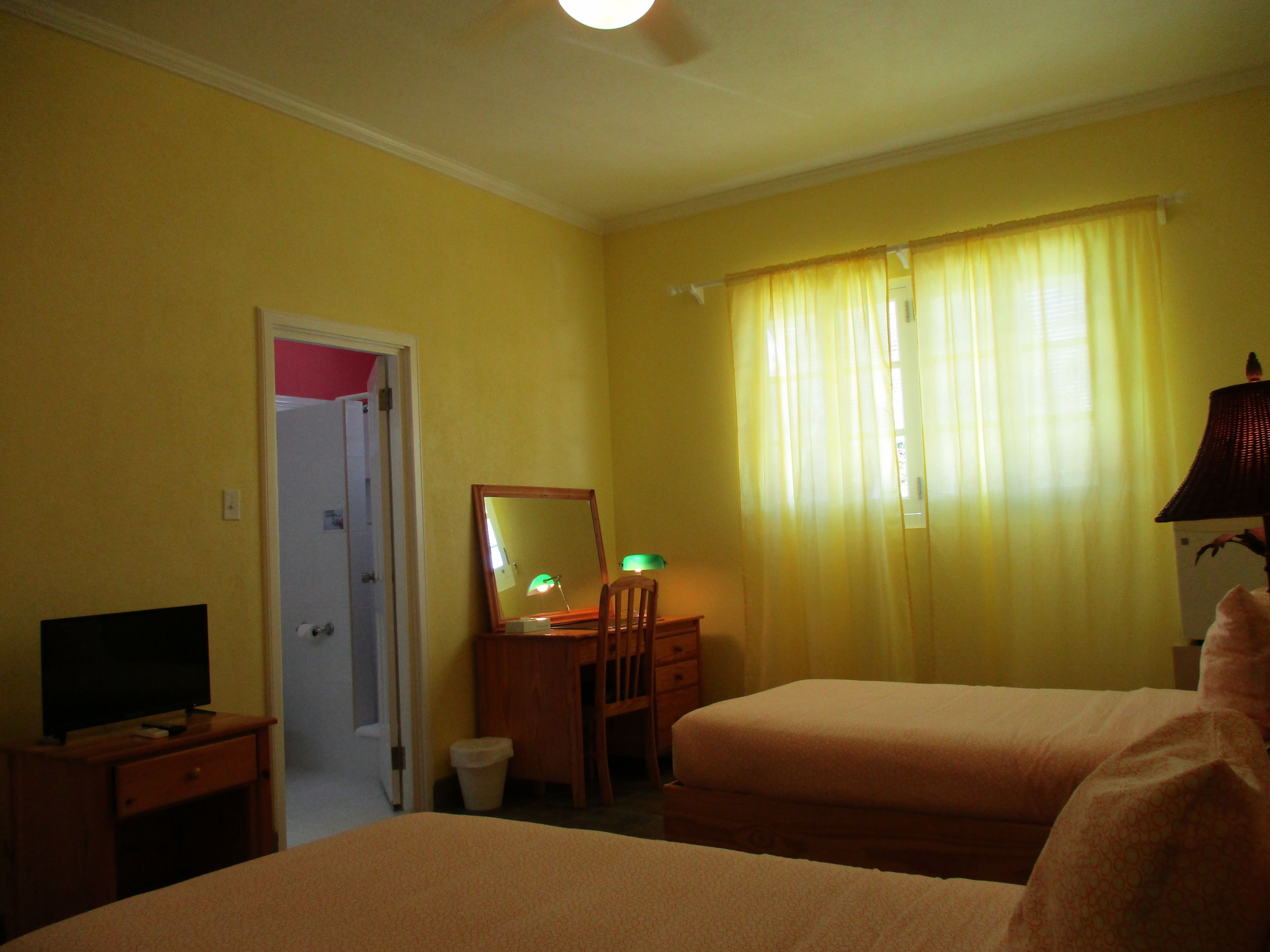 Una habitación de hotel con dos camas, un escritorio con lámpara, una silla, un espejo y una televisión.