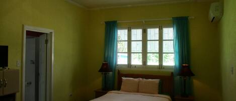 A bedroom with a bed, a ceiling fan, a window with curtains, and a nightstand with a lamp.
