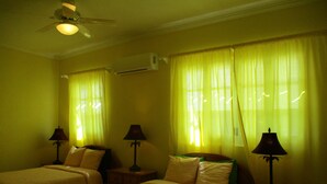 A hotel room with two beds, a ceiling fan, an air conditioning unit, and lamps on nightstands.