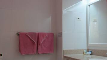 Un baño con inodoro, lavabo y espejo. Hay dos toallas rosas colgadas en la pared.